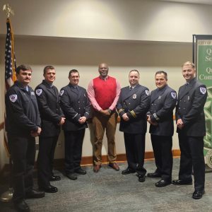 Chuck Grigsby stands in the center flanked by six new cadets standing in dress uniform.