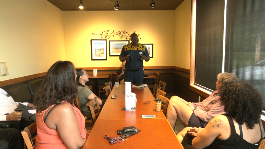 Mayor Pro Tem Chuck Grigsby standing at the end of a long table speaking to East Lansing residents seated at the table. (Photo credit: WLNS)